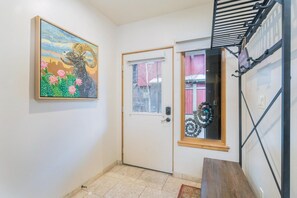 A hallway with a door, a painting, a window, and a bench.