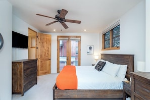 Une chambre à coucher avec un lit, des meubles en bois, un ventilateur de plafond, une télévision et une fenêtre.
