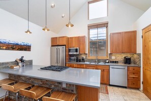 A modern kitchen with a large island, wooden cabinets, stainless steel appliances, and pendant lighting.