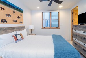 A bedroom with a bed, a ceiling fan, a window, and a TV.