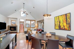 A spacious living area with a fireplace, a dining table, and a large abstract painting.