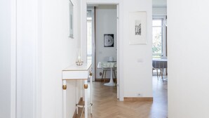 A hallway with a white table and chairs, a framed picture on the wall, and a door leading to another room. - Appartamento Volta 4 (Cernobbio)