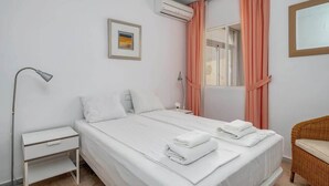 A neatly arranged hotel room with a bed, a nightstand, a lamp, a wicker chair, and a window with curtains. - Seaview Balcony by Costarentals - Ref 203 (Mijas)