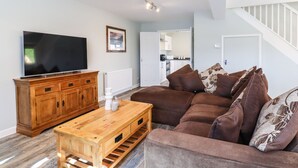 A living room with a wooden coffee table, a brown sofa, a flat-screen TV, and a staircase leading to an upper level. - Orchard Retreat (Tonbridge)