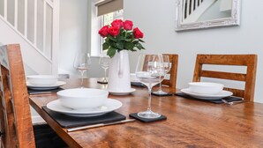 A dining table set with white plates, bowls, and wine glasses, accompanied by a vase of red roses. - Orchard Retreat (Tonbridge)