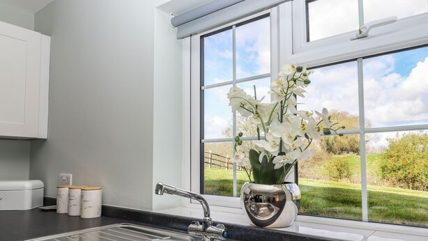 A kitchen with a stainless steel sink, a window with a view of greenery, and a vase with white flowers. - Orchard Retreat (Tonbridge)