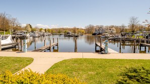 A marina with boats docked, a grassy area in the foreground, and houses in the background.