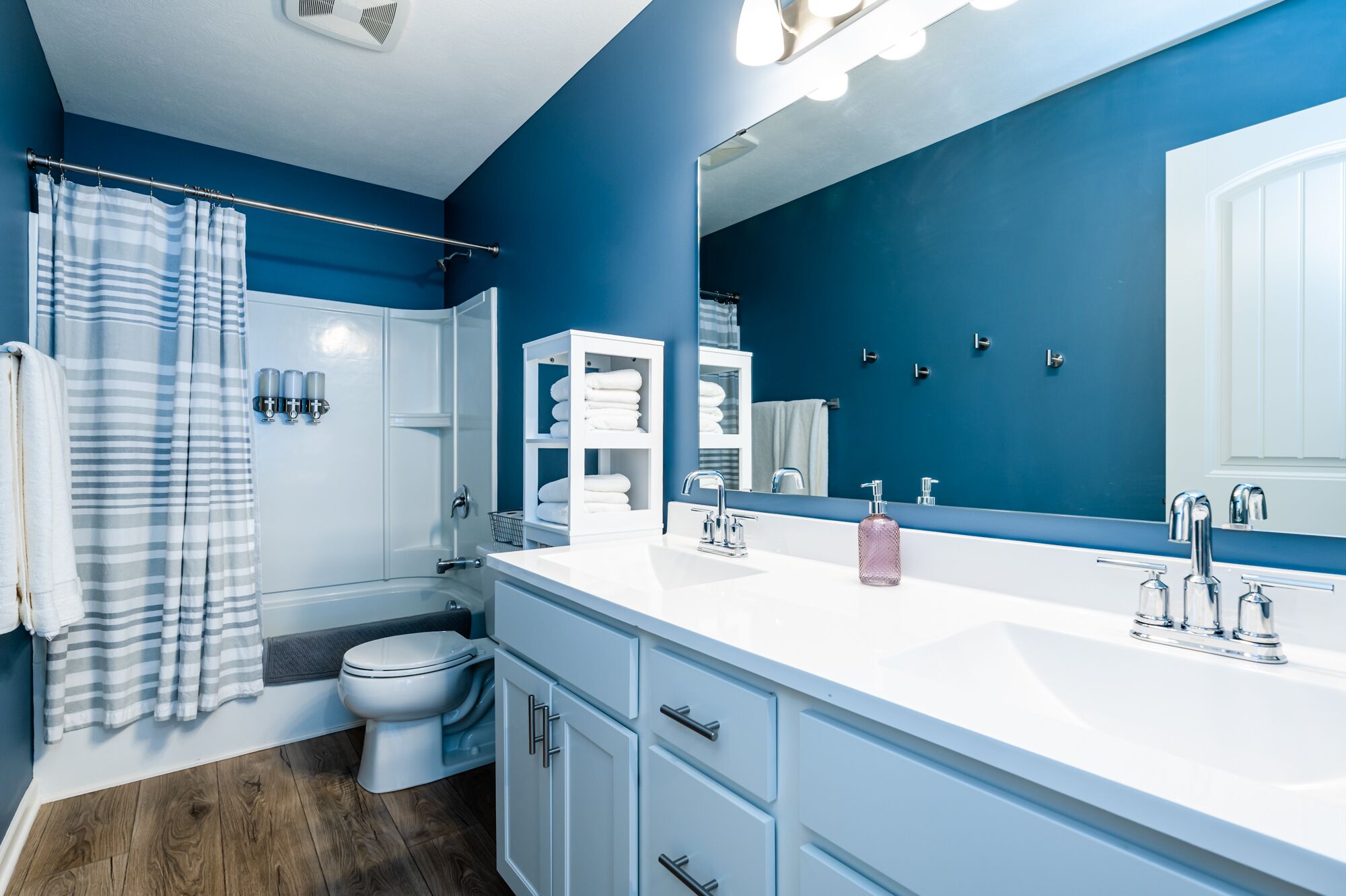 A modern bathroom with a blue wall, white fixtures, a large mirror, and a shower curtain.