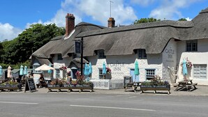 En traditionel bygning med stråtækt tag og et skilt, der viser "The Castle Inn Pub & Rooms".