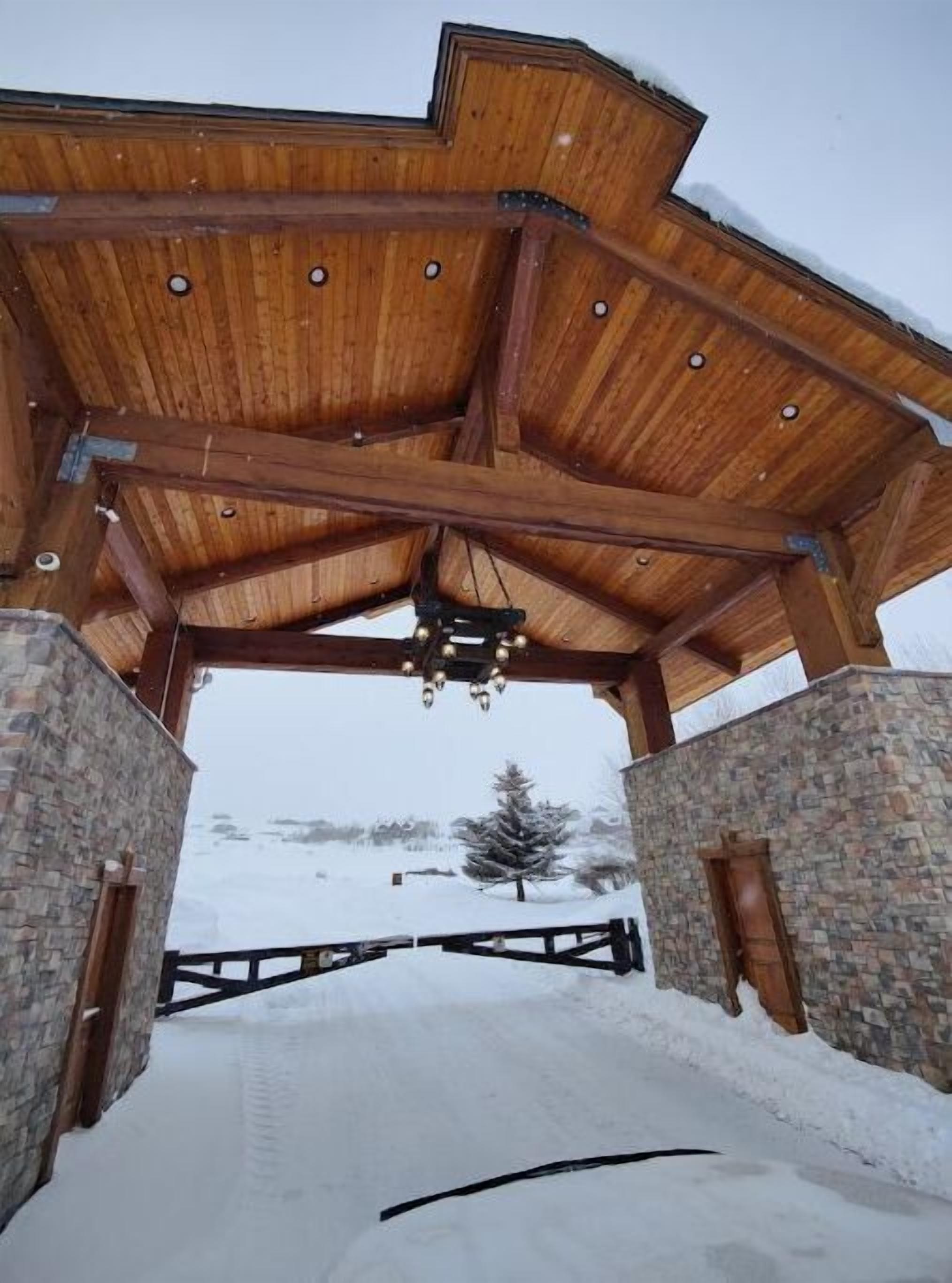 A wooden pavilion with a sloped roof, stone walls, and a snow-covered ground.