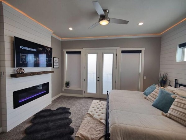 A bedroom with a TV, fireplace, ceiling fan, and a large bed. - Panoramic Lake Views, Pool, Hot Tub, Gameroom! (Fish Haven)