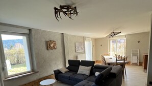 A spacious living room with a sectional sofa, a dining table with chairs, and a view of the outdoors. - Gîte à Saulxures sur Moselotte à 1 min du lac (Saulxures-sur-Moselotte)