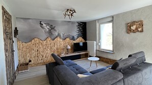 A modern living room with a large gray sectional sofa, a flat-screen TV, and a mural of a wolf on the wall. - Gîte à Saulxures sur Moselotte à 1 min du lac (Saulxures-sur-Moselotte)