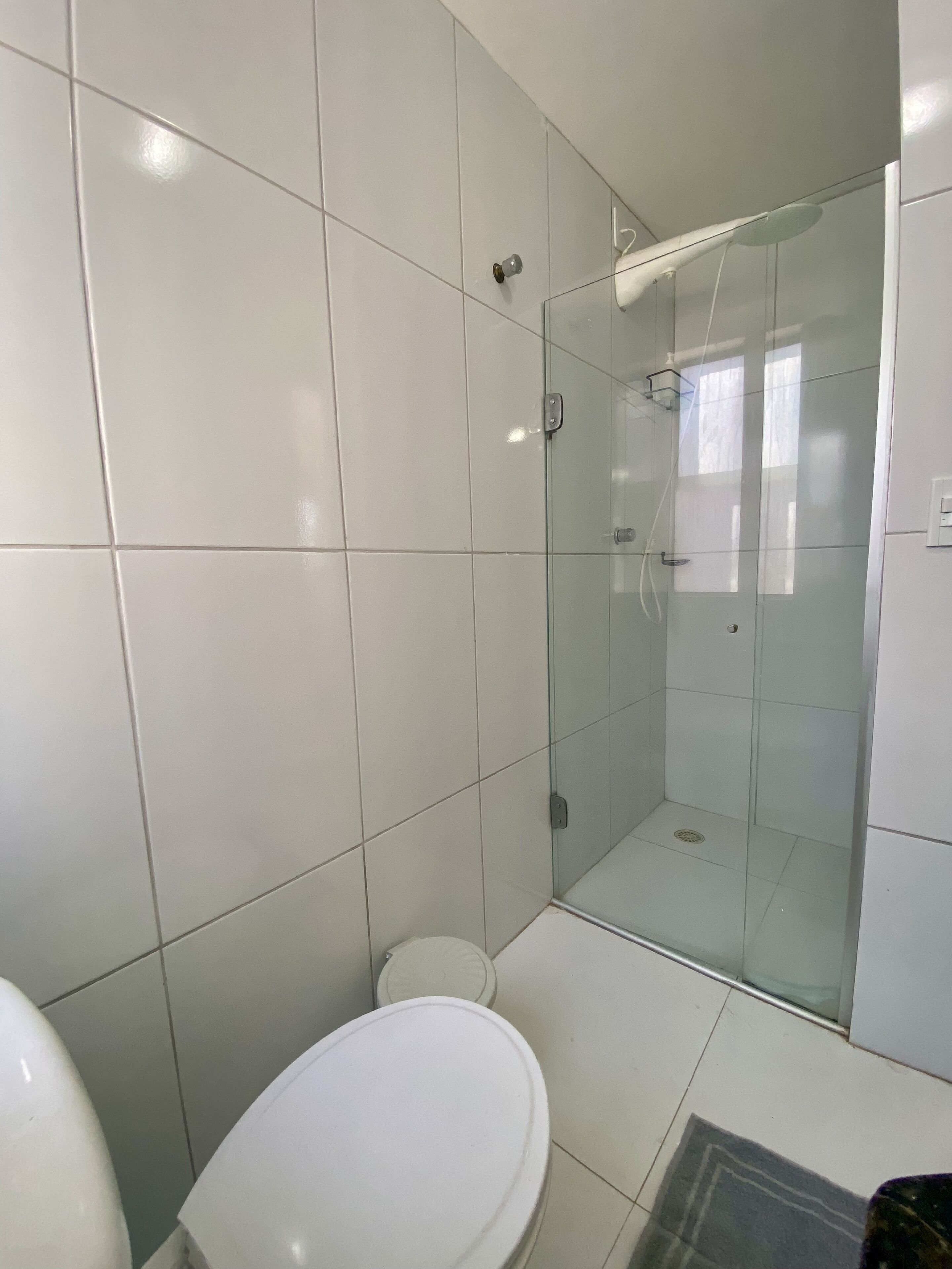 Un baño moderno con azulejos blancos, cabina de ducha de vidrio y un inodoro.
