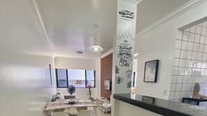 A modern kitchen with a dining area, featuring a kitchen island with stools, a large window, and a decorative wall sign. - Ametista 2 (Maceió)