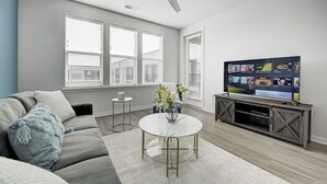 A modern living room with a grey sofa, a round coffee table, and a flat-screen TV on a wooden stand. - *LUXURIOUS 1BED/1BATH - KING BED* -POOL (Fishers)