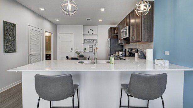 A modern kitchen with a white island, two bar stools, pendant lighting, and dark wooden cabinets. - *LUXURIOUS 1BED/1BATH - KING BED* -POOL (Fishers)