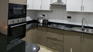 A modern kitchen with stainless steel appliances, white cabinets, and a black countertop. - Breezeskyline with greenery view (Kiambu)