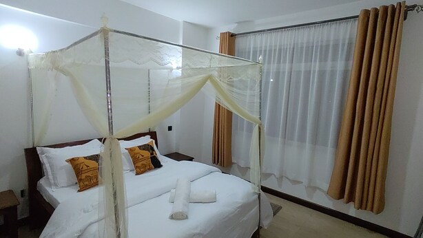 A hotel room with a four-poster bed, a nightstand, a window with curtains, and a bedspread. - Breezeskyline with greenery view (Kiambu)