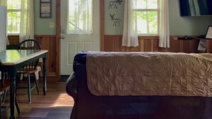 Interior de cabana com teto de madeira, um sofá, mesa de jantar com cadeiras e uma TV fixada na parede.
