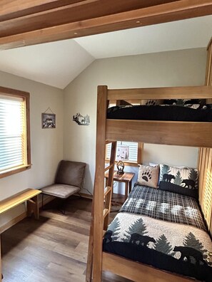 A bunk bed with a forest-themed bedding, a wooden desk, a chair, and a small table with a lamp. - Wilderness Retreat (Cadiz)
