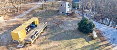 A rustic cabin with a deck and a small shed, surrounded by trees and a clear path.