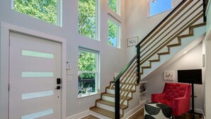 A modern interior with a staircase, a red chair, and a window with a view of trees.