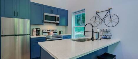 A modern kitchen with blue cabinets, stainless steel appliances, a large island, and a bicycle decoration on the wall.
