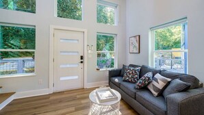 Un salon spacieux avec un canapé gris, de nombreuses fenêtres et un plancher en bois.