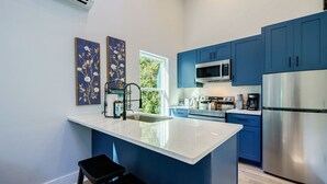 A modern kitchen with blue cabinets, stainless steel appliances, and a central island with a sink and stools.