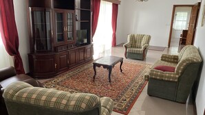 A living room with a dark wooden cabinet, a television, a coffee table, and two green armchairs with red cushions. - Green Tropical House ,Great view of the ocean (Ponta Delgada)