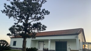 A white building with a red-tiled roof, a front door, and a garage. - Green Tropical House ,Great view of the ocean (Ponta Delgada)