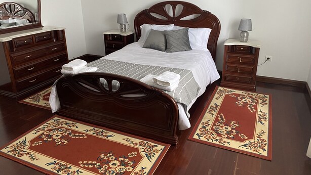 A neatly arranged bedroom with a wooden bed, two nightstands, a dresser, and a mirror. - Green Tropical House ,Great view of the ocean (Ponta Delgada)