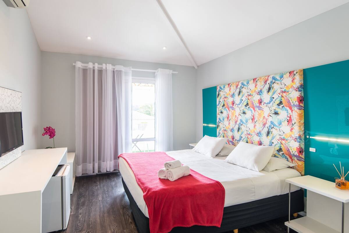 Une chambre d’hôtel moderne équipée d’un lit, d’un bureau, d’une télévision et d’une fenêtre avec des rideaux.