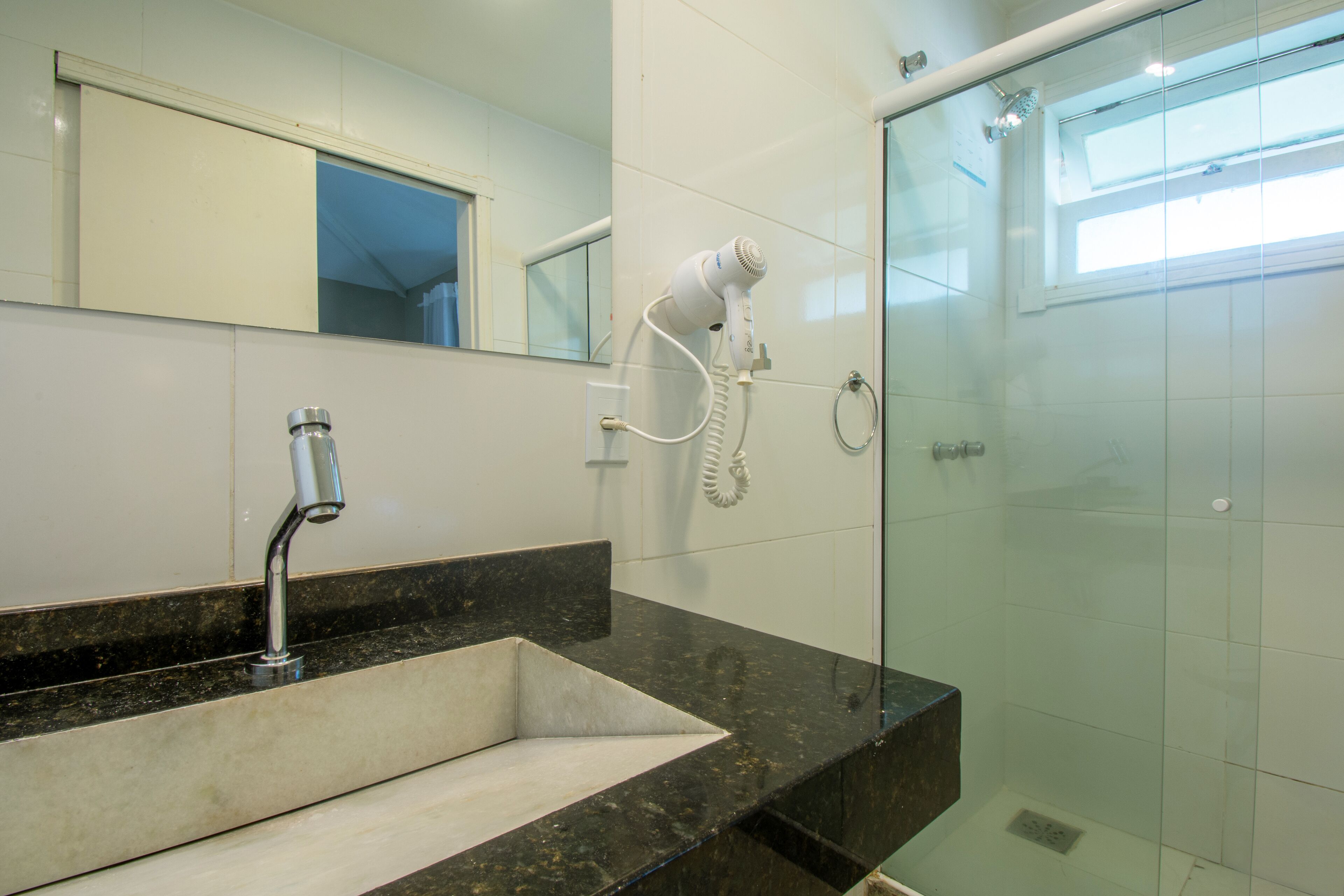 Une salle de bain équipée d’un lavabo, d’un miroir, d’un sèche-cheveux et d’une douche à parois de verre.