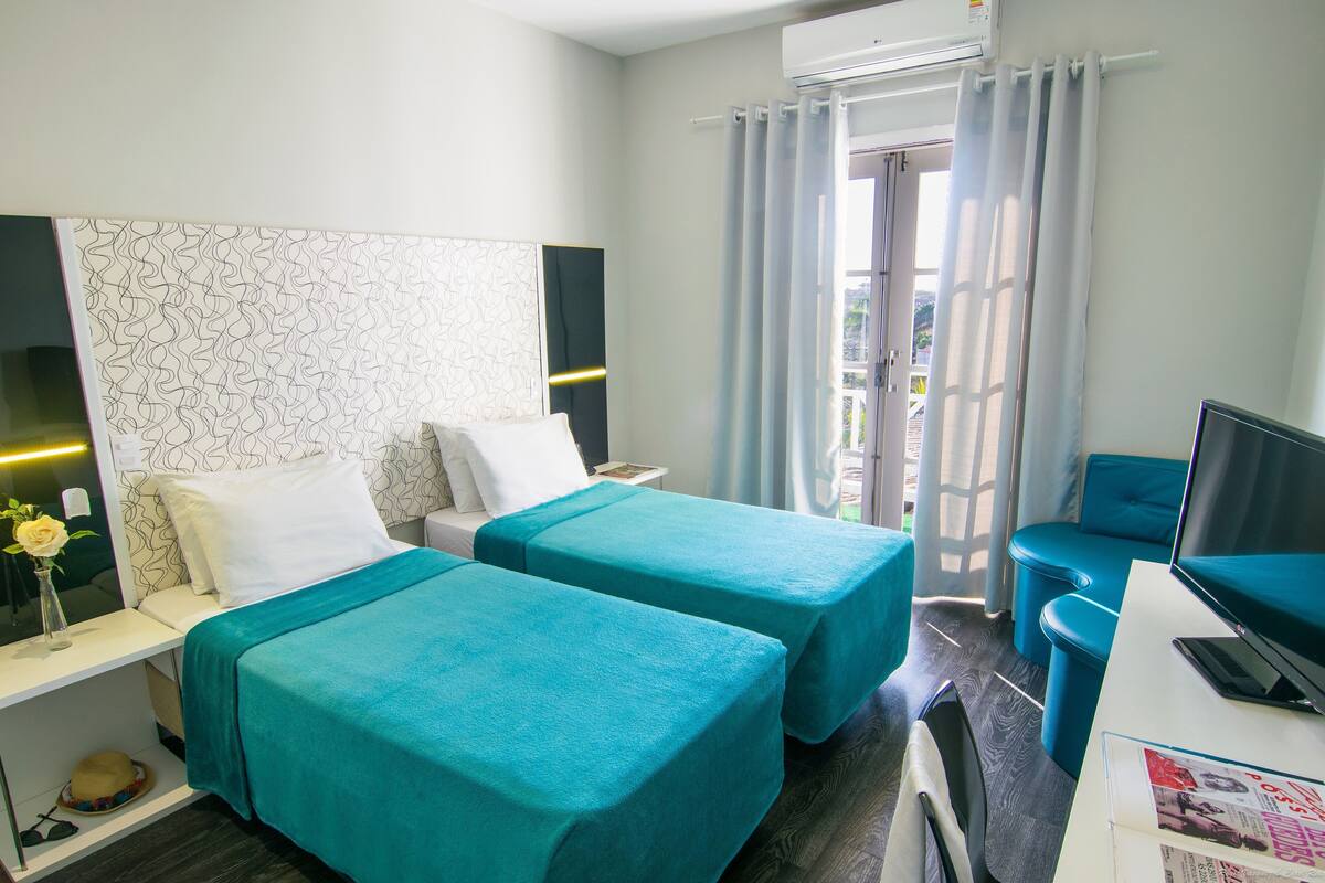 Une chambre d’hôtel avec deux lits, un bureau avec un ordinateur, une télévision et une fenêtre avec des rideaux.