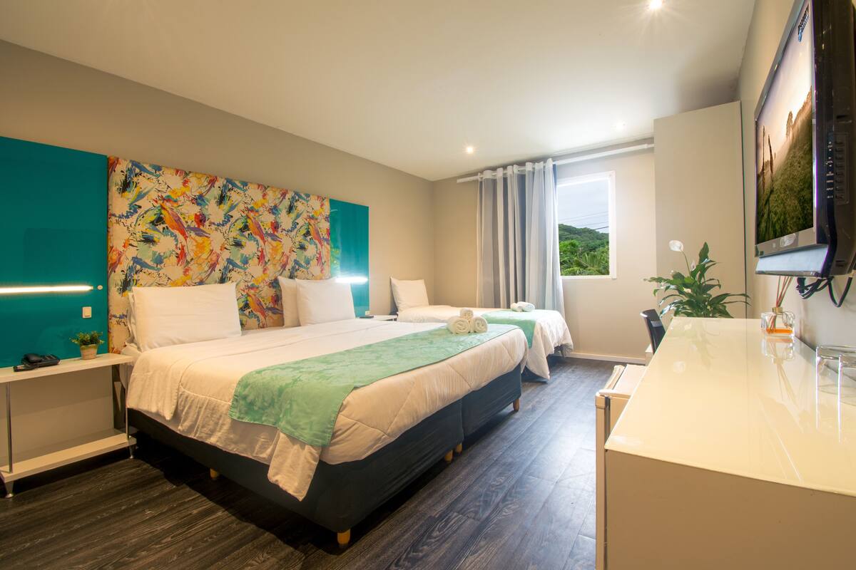 Une chambre d’hôtel moderne avec deux lits, une grande peinture abstraite, un téléviseur à écran plat et une vue sur l’extérieur.