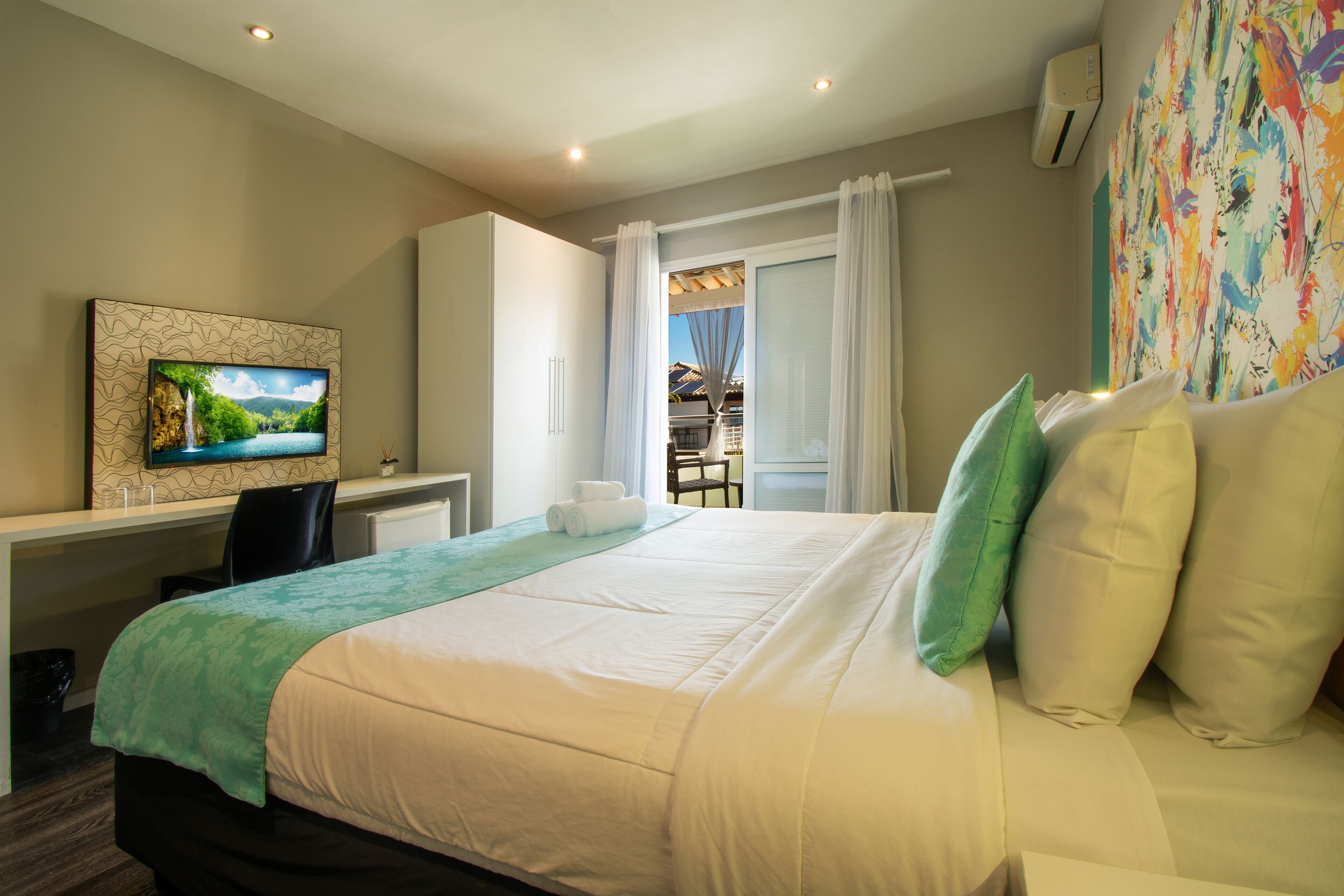 A hotel room with a bed, a desk, a TV, and a view of the outside.