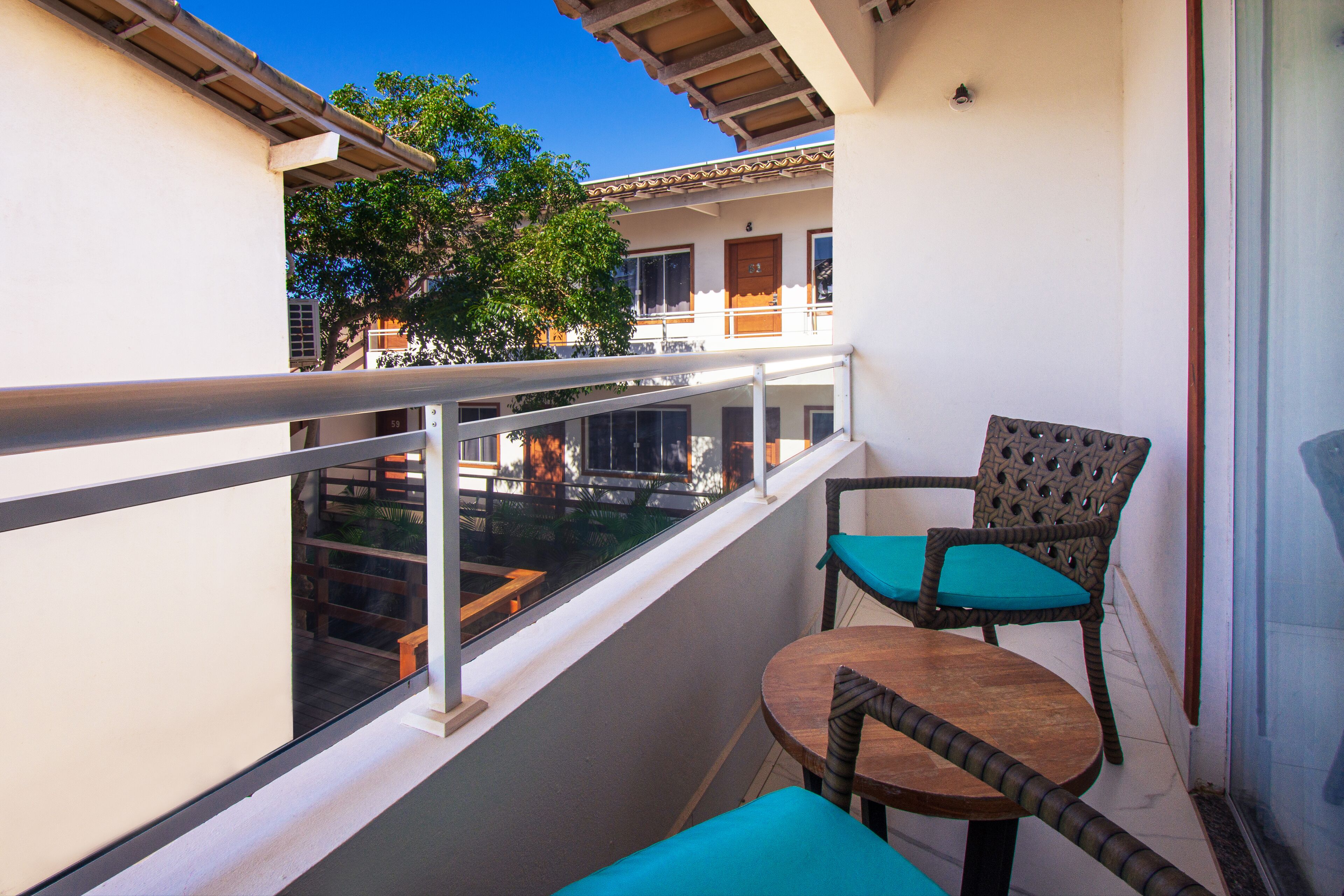 A balcony with a glass railing, two wicker chairs with blue cushions, and a small round table.