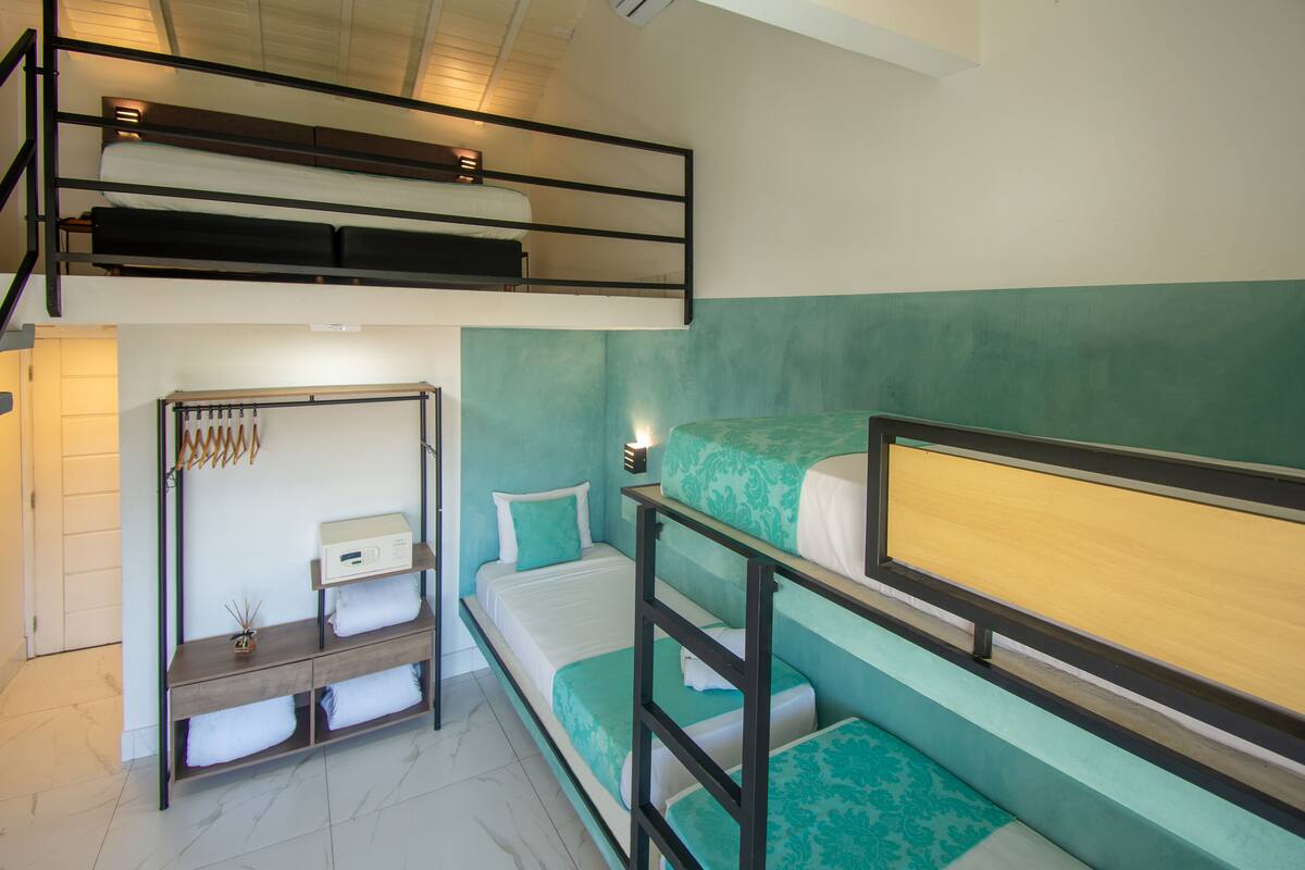 Une chambre avec un lit superposé, un bureau intégré et une étagère, une petite table de chevet et une lampe fixée au mur.
