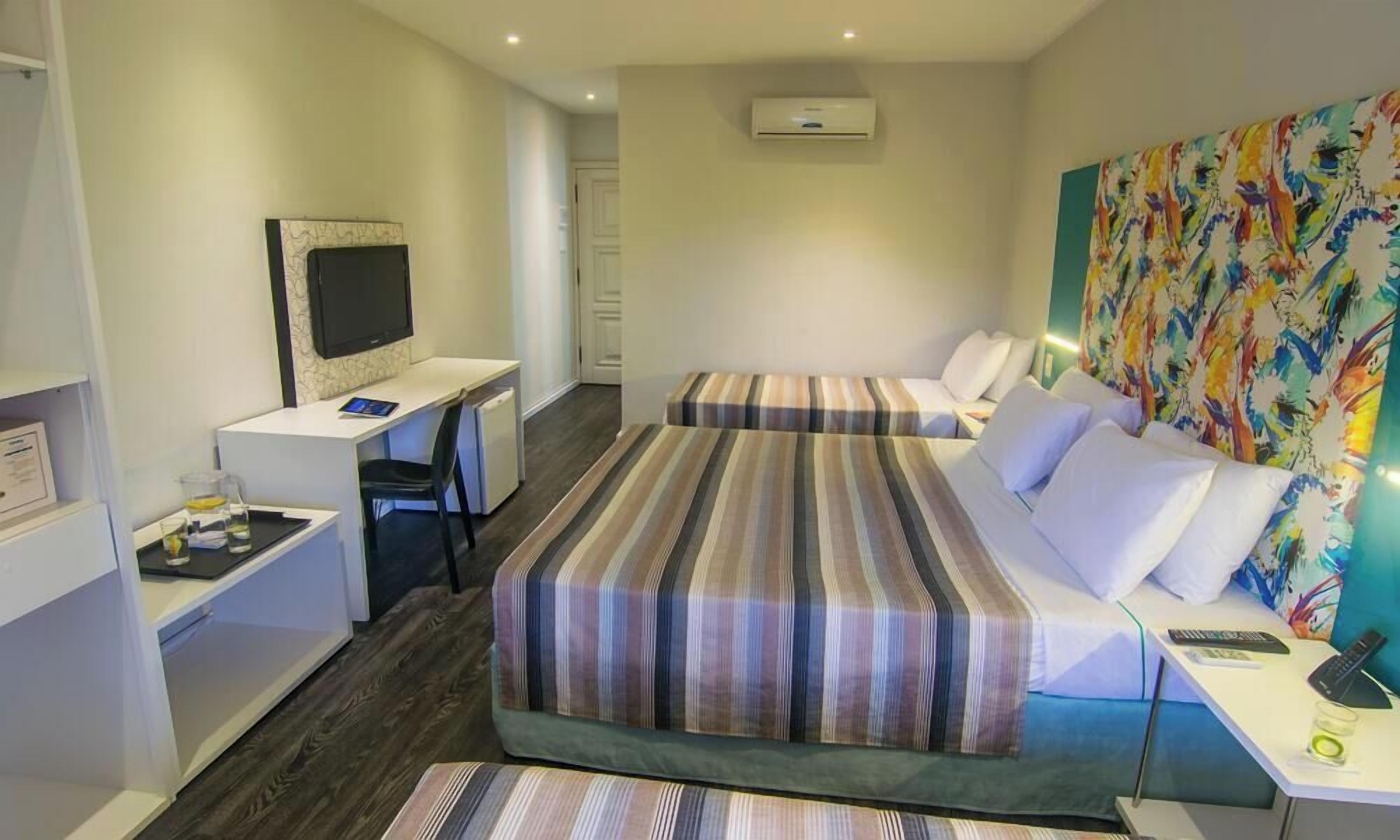 Ein Hotelzimmer mit zwei Betten, einem Schreibtisch, einem Sessel, einem Fernseher und einer Klimaanlage.
