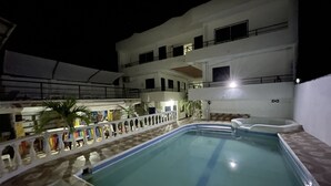 A swimming pool with a tiled deck, surrounded by a white building with multiple balconies and windows. - Hotel cabañas de TOLÚ  (Sucre)
