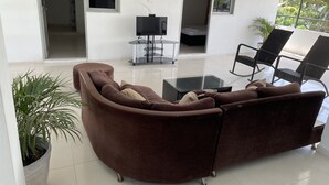 A modern living room with a brown sectional sofa, a glass coffee table, and black chairs. - Hotel cabañas de TOLÚ  (Sucre)