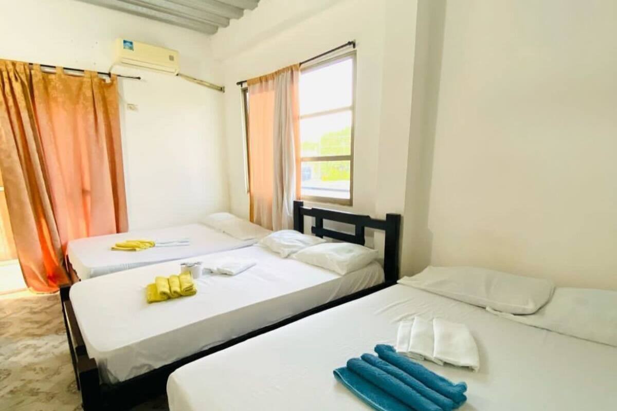 Ett hotellrum med två separata sängar, ett fönster med gardiner, en luftkonditioneringsanläggning och en mönstrad matta.