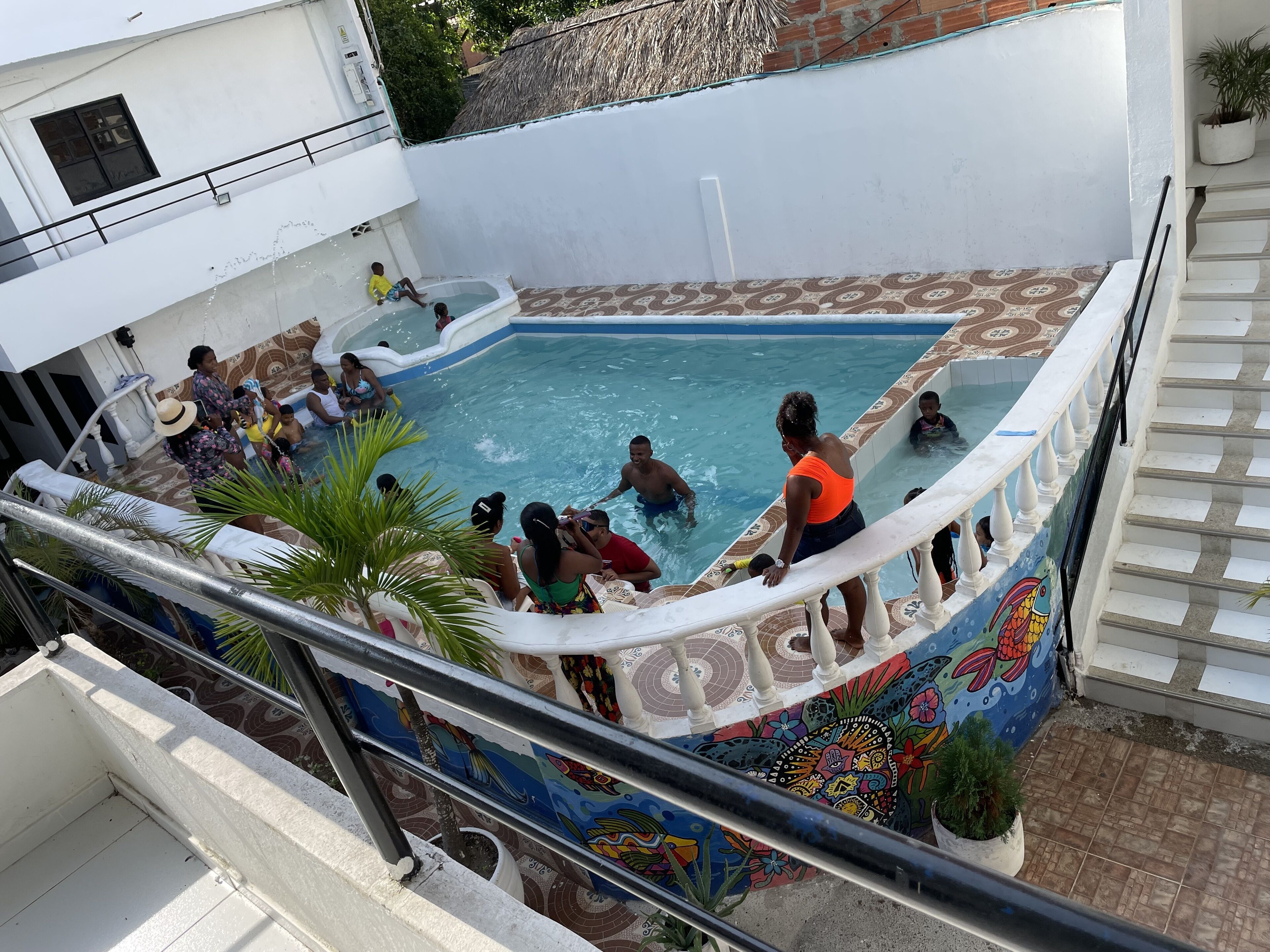 A swimming pool with people enjoying the water, surrounded by a white building with a colorful mural.