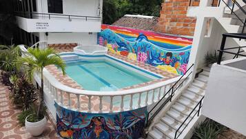Una piscina con un mural colorido, rodeada de plantas en macetas y una escalera.