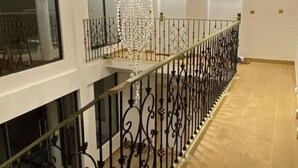 Un intérieur spacieux avec un plancher en bois, une rampe décorative en métal et un luminaire suspendu.