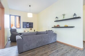 A living room with a grey sofa, a flat-screen TV, a ceiling fan, and wooden flooring.