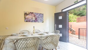 Un comedor con una mesa dispuesta para cuatro personas, sillas, un cuadro en la pared y una puerta que da al exterior.