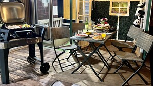 Un espace extérieur aménagé pour les repas, avec un barbecue, des chaises en osier et une table dressée pour un repas.
